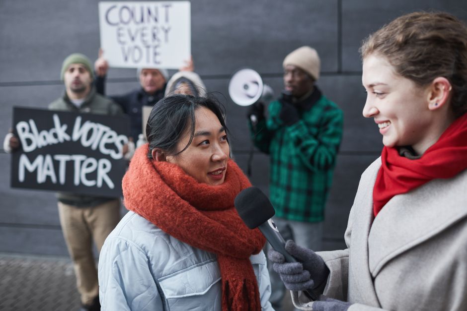 A reporter interviews a protestor at a street demonstration highlighting voting rights issues.