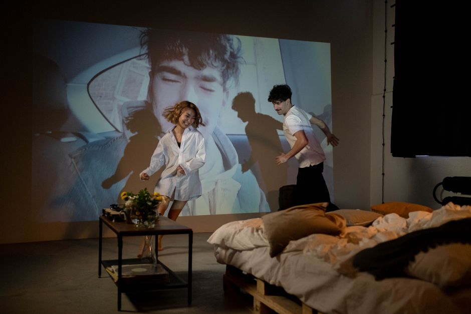 A young couple having fun and being playful while projecting a movie in their cozy bedroom setting.
