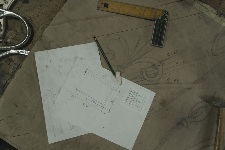 Detailed view of architectural sketches and drawing tools on a workbench, reflecting a crafting workspace.