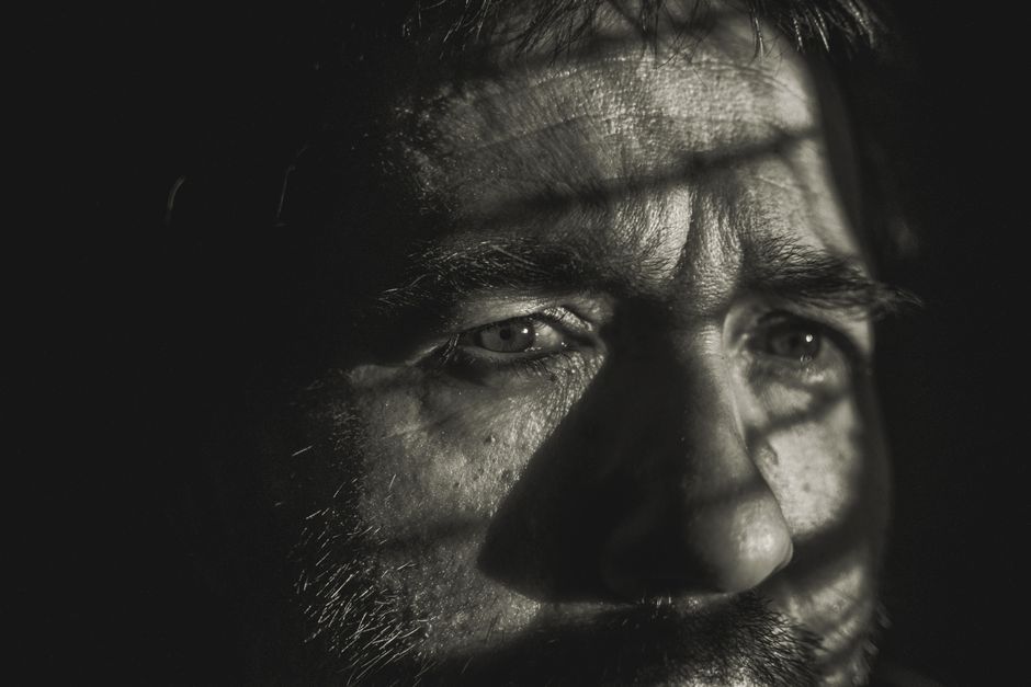 A dramatic black and white portrait of a pensive man in deep thought, showcasing textured light and shadow.
