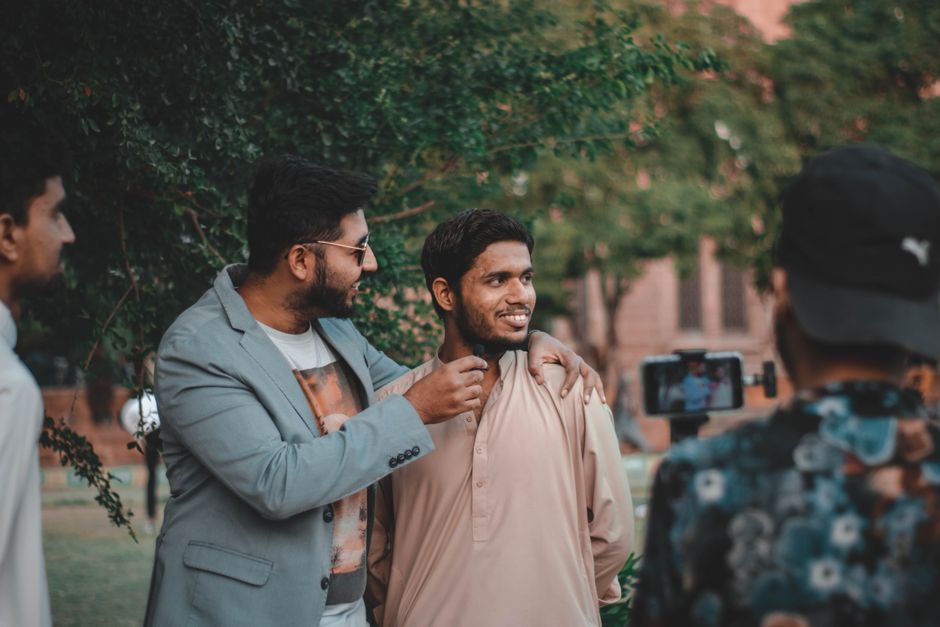 Two men casually interacting outdoors with a live recording setup, surrounded by greenery.