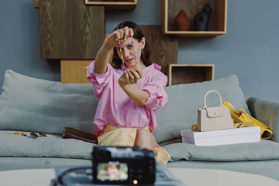 Woman in pink blouse displaying colorful jewelry for vlogging indoors.