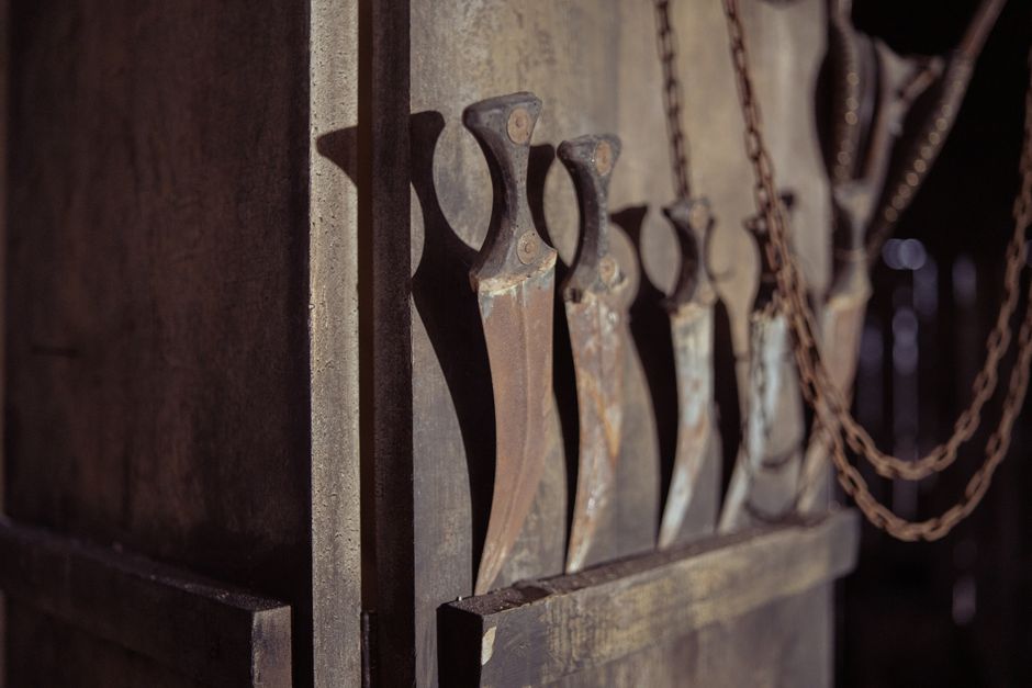 Close-up of vintage rusty knives hanging on a wall in a dimly lit workshop.