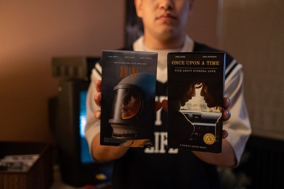 A person holding vintage VHS tapes in a cozy indoor setting.