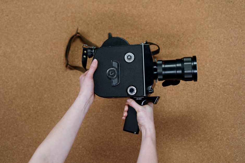 A person holds a vintage cinema camera over a corkboard background, showcasing a retro aesthetic.