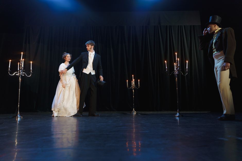 Period drama actors perform an elegant candlelit scene on stage.