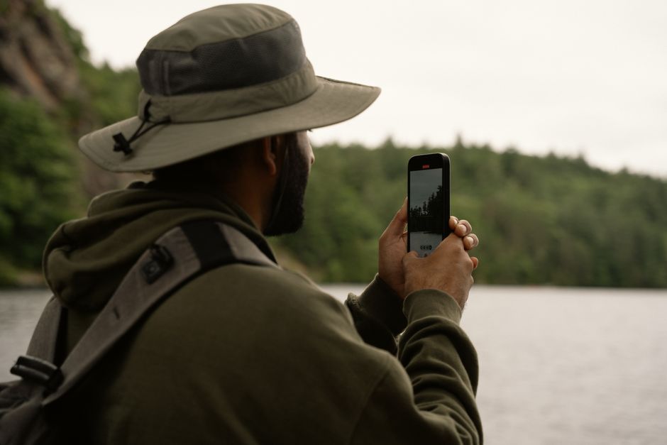 Person outdoors taking a photo of lake scenery with a smartphone.