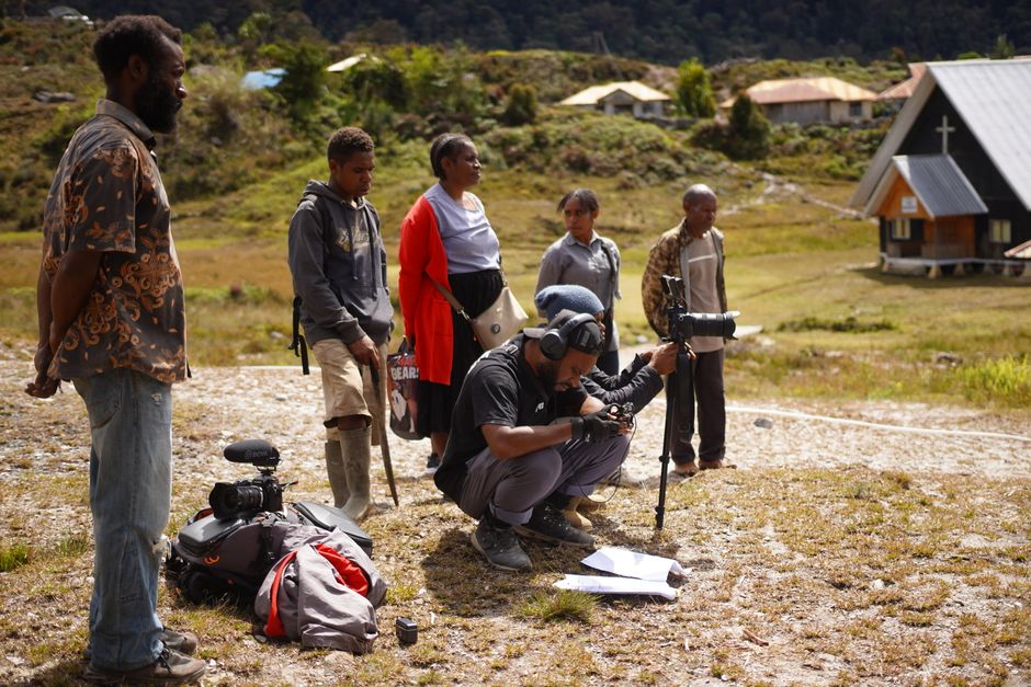 A film crew setting up equipment outdoors in a rural village in Papua, Indonesia.