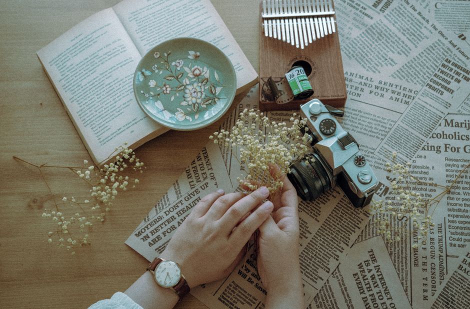 A vintage flat lay composition featuring an old camera, flowers, book, and ceramic plate.