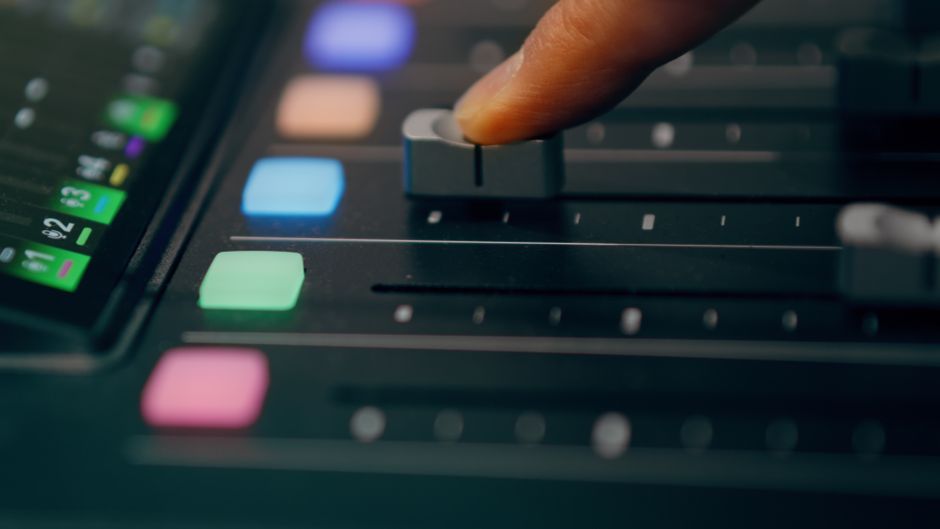Close-up of a finger adjusting an audio mixer slider with colored buttons, highlighting sound studio equipment.