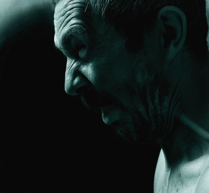 Dramatic side view of a man expressing intense emotion in dark, moody lighting.