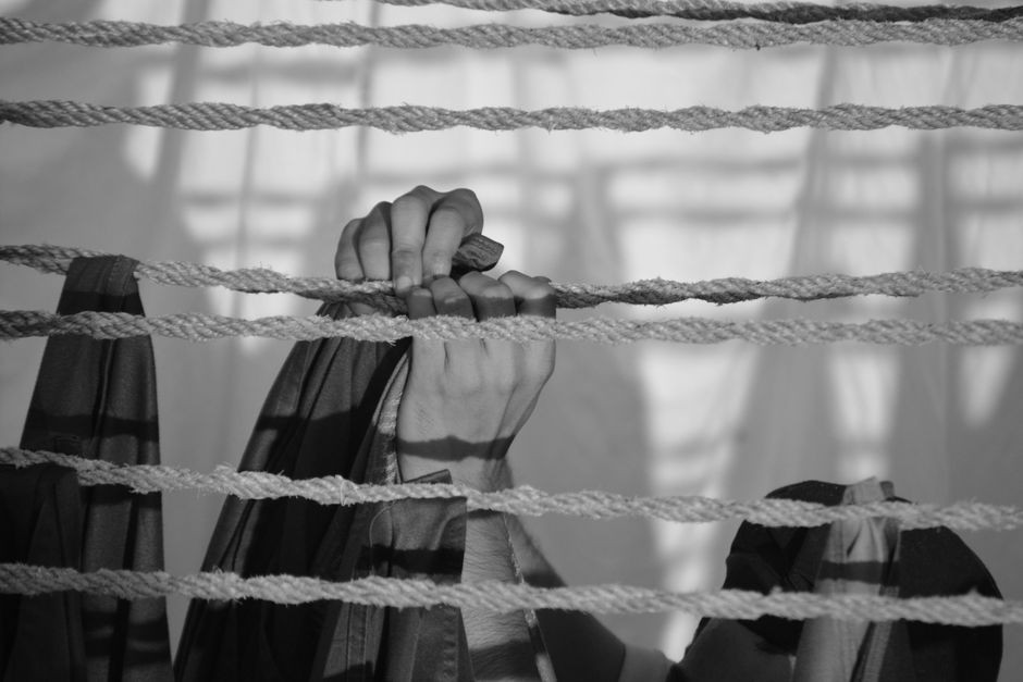 Monochrome image of hands clutching ropes, casting shadows, creating a dramatic effect.