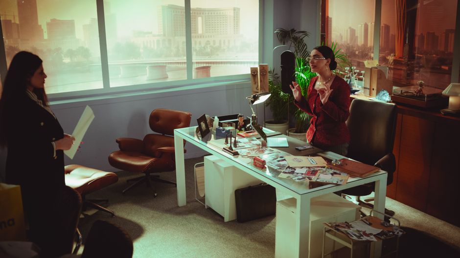 Two professional women engage in a business meeting in a modern Baghdad office with a view.