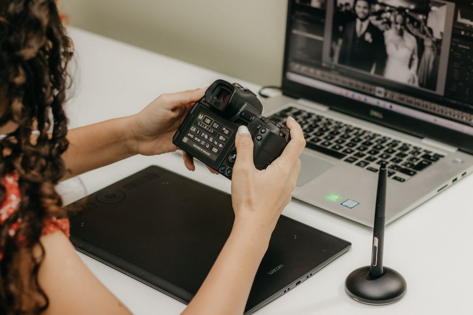 Photographer holding a camera, editing photos on a laptop using Adobe Lightroom with a stylus and tablet.