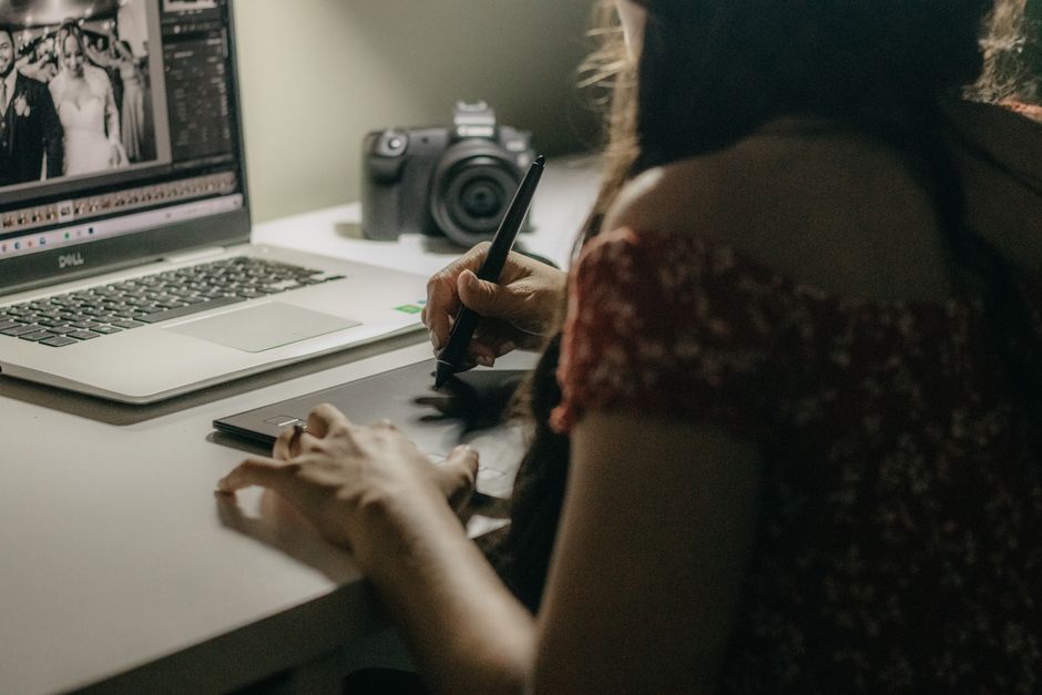 A woman edits photos on a tablet and laptop in a creative workspace.