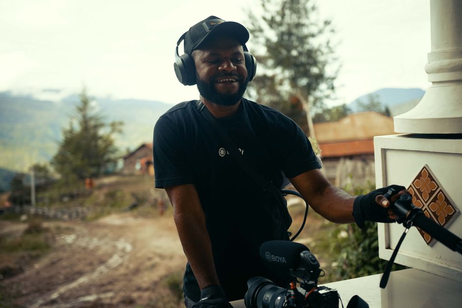 A videographer works with equipment outdoors in a beautiful mountain setting.