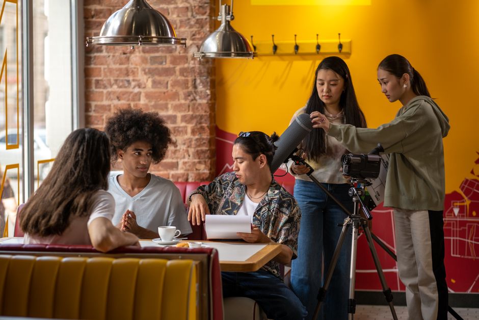 A diverse film crew collaborating in a cozy cafe setting with cameras and microphones.