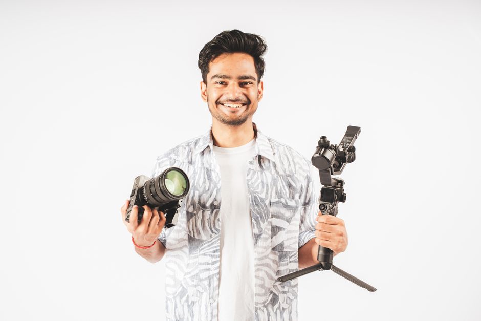 Smiling young man holding a professional camera and gimbal, showcasing videography equipment.