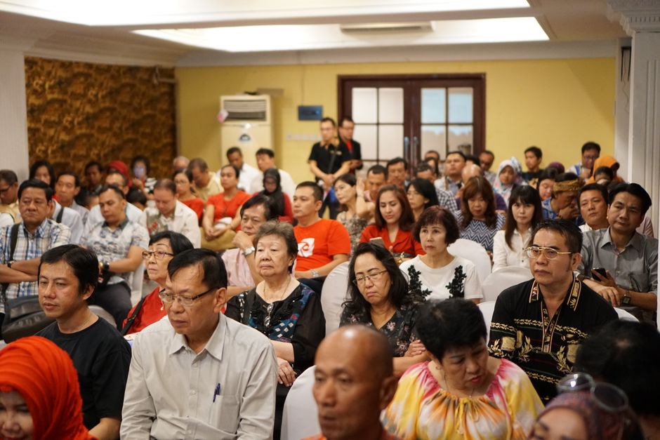 A diverse group of adults attending a conference in an Indonesian indoor setting.