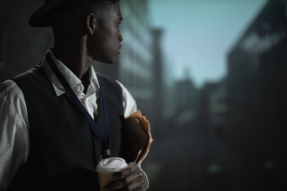 A contemplative man in an urban setting dressed as a detective, holding documents and coffee.