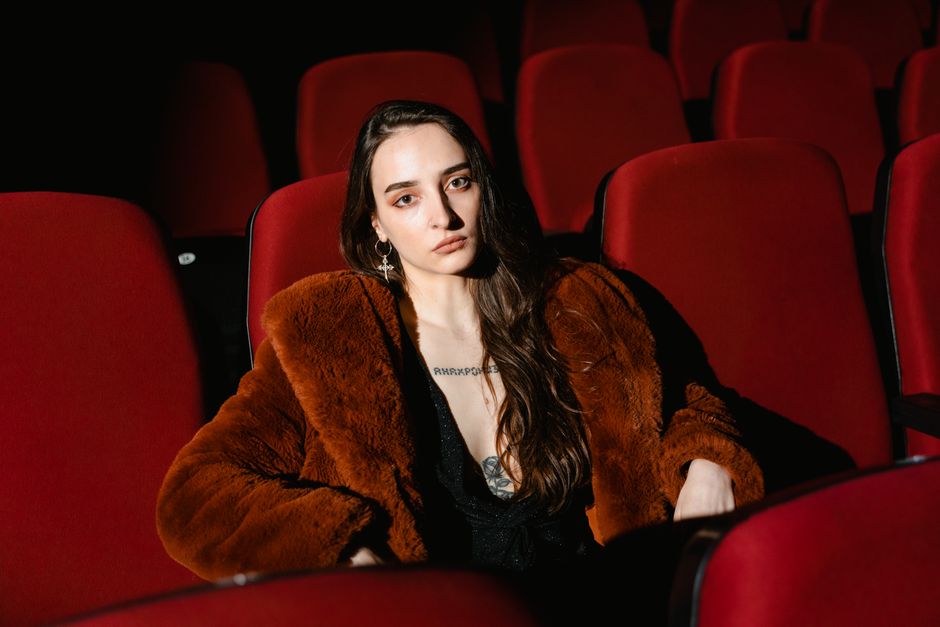 A woman sitting alone in a cinema with red seats, exuding a contemplative mood.