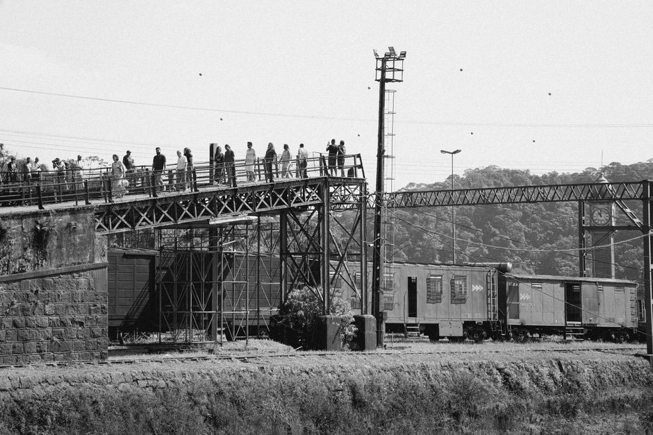Monochrome image of people standing on a railway overpass with a passing train below.