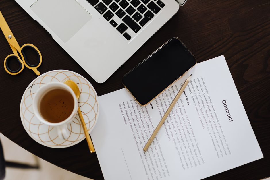 Top-view of a workspace with contract, coffee, laptop, and smartphone focused on business productivity.