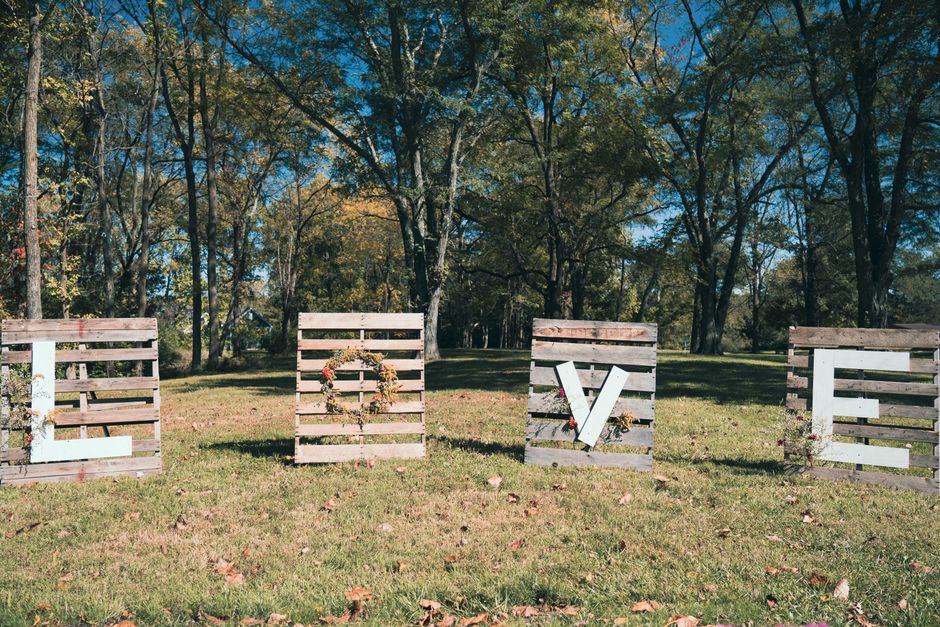 Wooden LOVE letters on grass with forest backdrop, ideal for fall wedding decor.