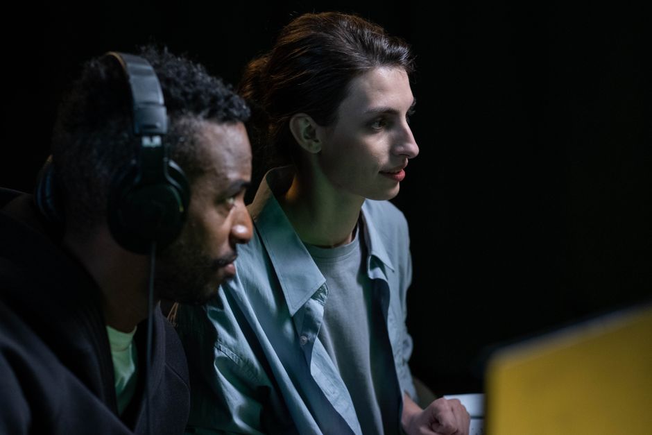 Two people working together with headphones and screens, deeply focused on collaborative tasks in a low-light setting.