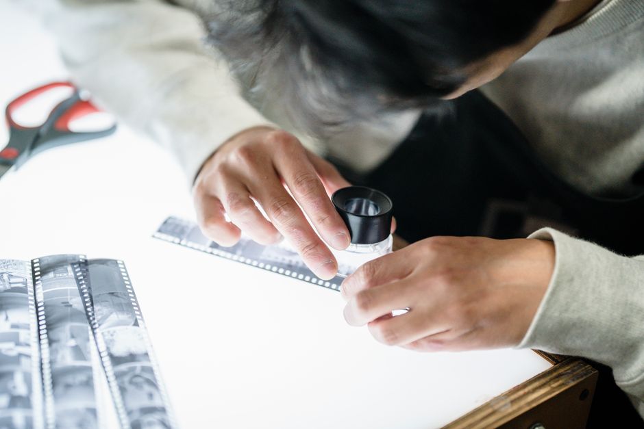 Photographer scrutinizing film negatives on a lightbox using a magnifying glass, focusing on details.