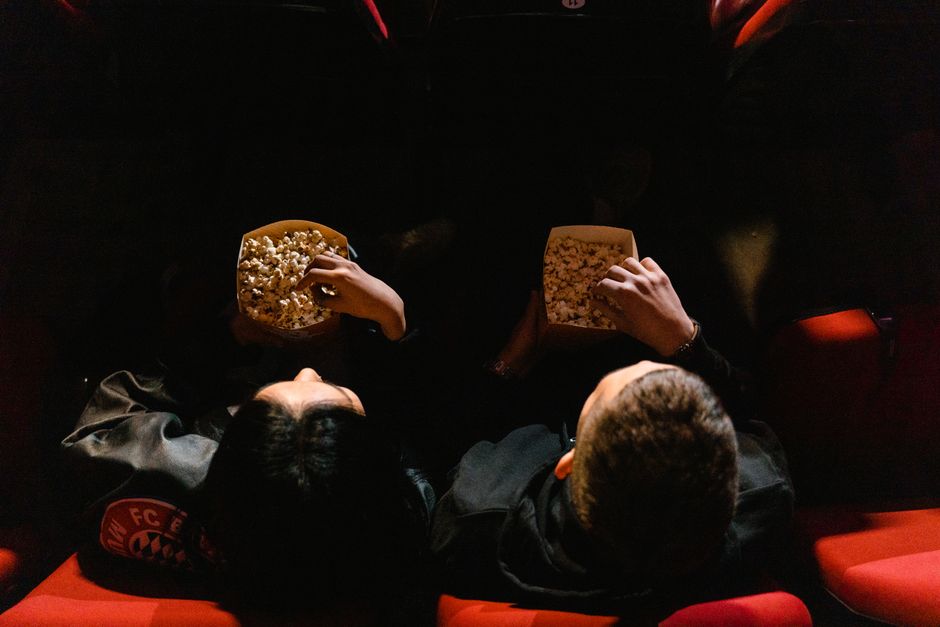 A couple sitting close together in a cinema, sharing popcorn from an overhead perspective.