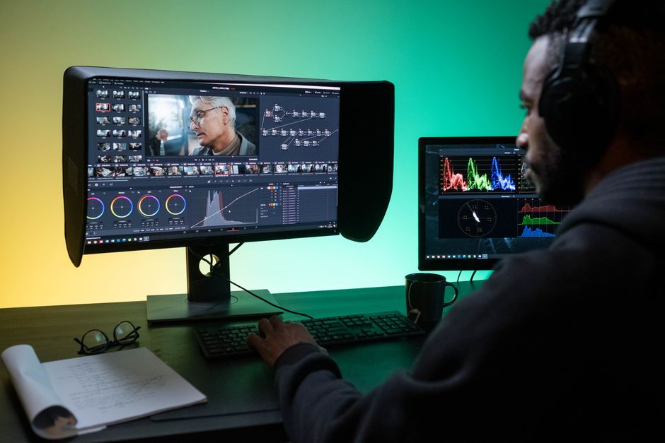 Man editing footage on dual monitors in a modern studio setting.