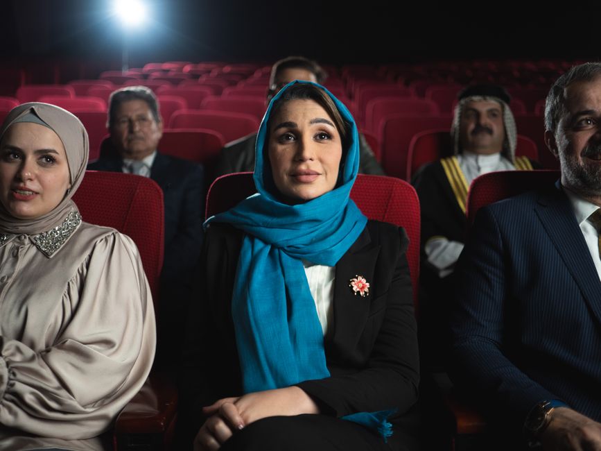A diverse group of people enjoying a cinematic experience inside a Baghdad theater. Captured in vivid detail.