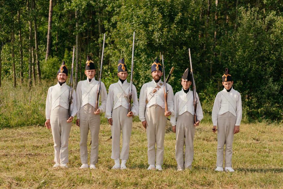 A group of men in white uniforms participate in a Napoleonic war reenactment outdoors.