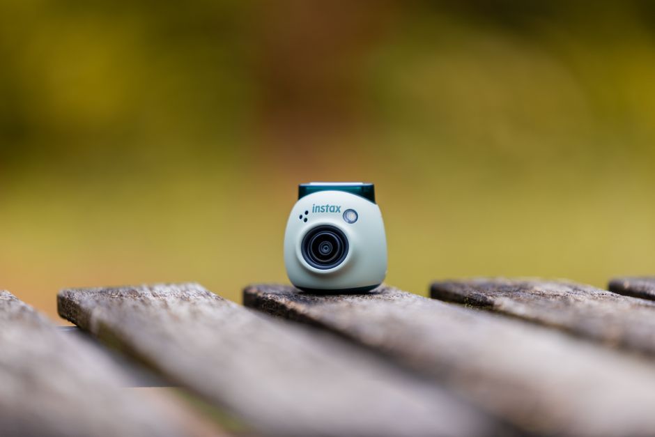 A mini Instax camera sits on a rustic wooden surface with a blurred background, highlighting its elegant design.