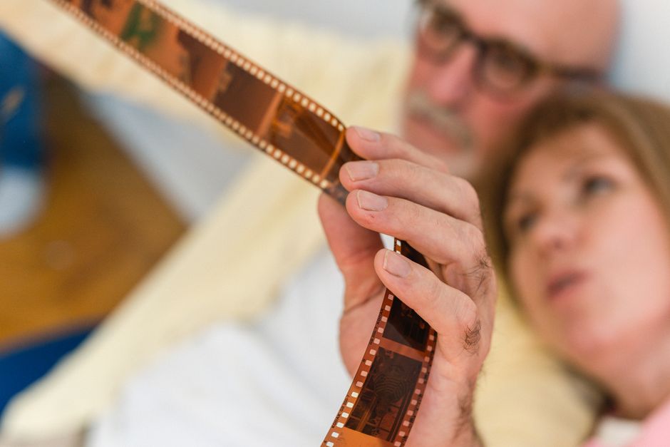 An elderly couple intently examining an old photographic film strip together indoors.