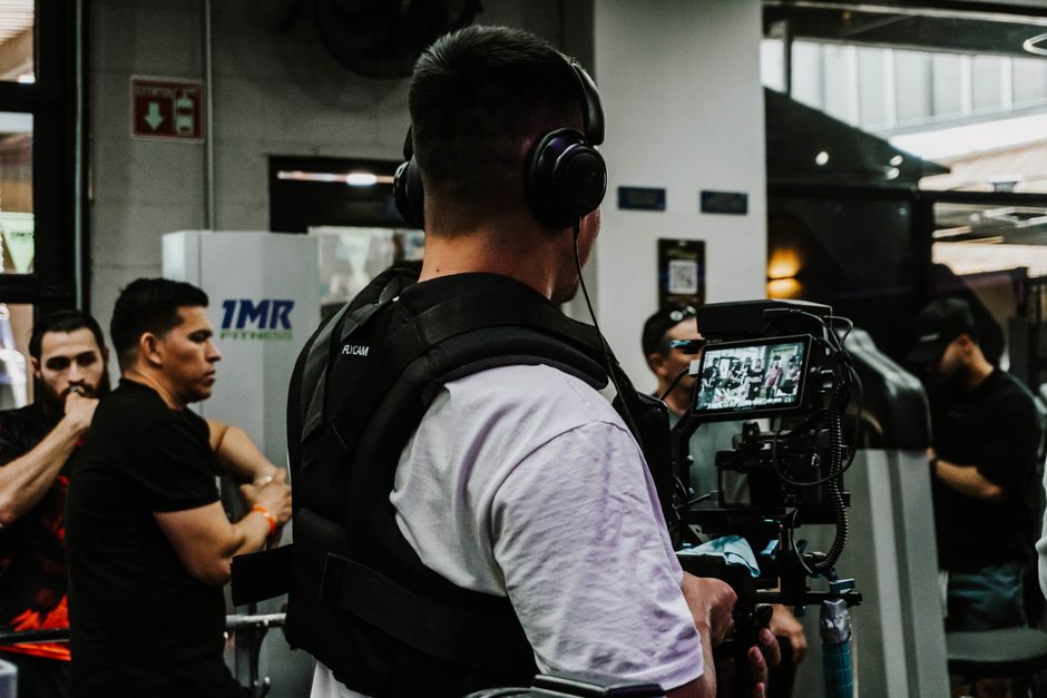 Back view of a filmmaker using a camera rig indoors with a focus on capturing event activities.