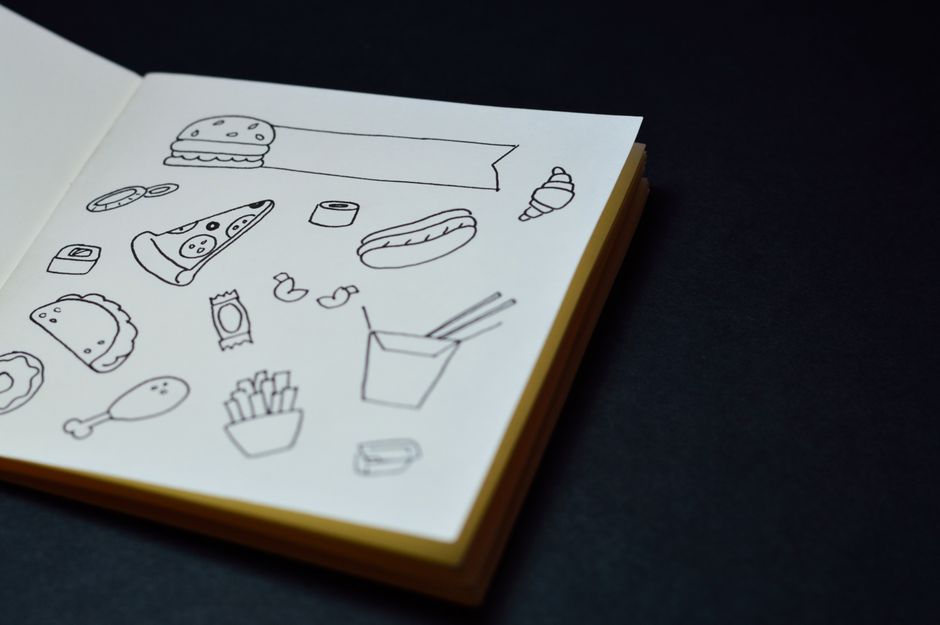 Open sketchbook displaying hand-drawn food doodles like pizza, burger, and fries.