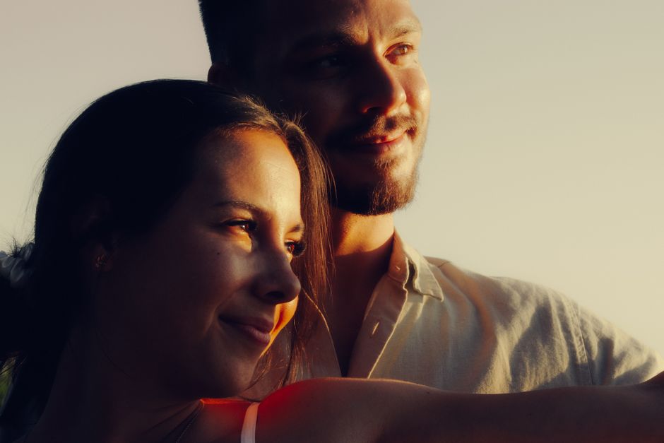 A couple gazing affectionately at a sunset, bathed in warm, natural light.