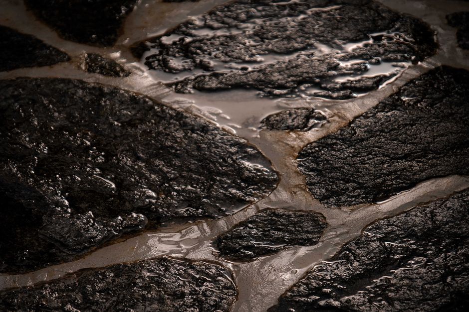 From above of tiny narrow brooks on surface of rough uneven wet large stone in daylight