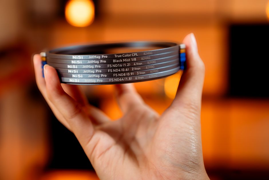 Close-up of a hand holding NiSi camera filters against a warm, blurred studio background.