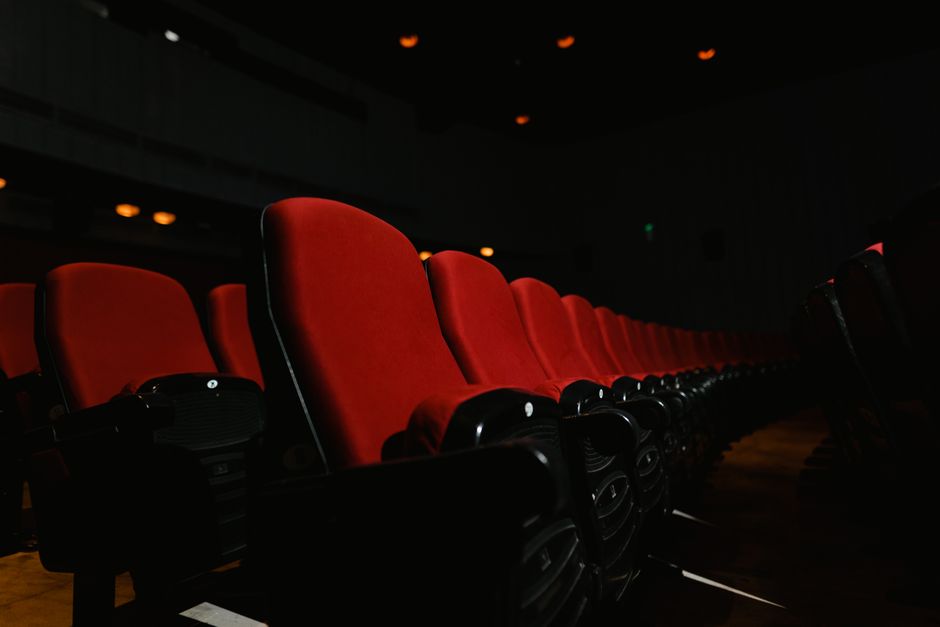 A close-up of empty red seats in a dark movie theater, emphasizing solitude and anticipation.