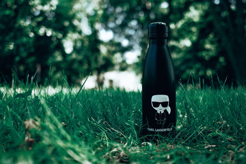 Stylish black water bottle sitting on a verdant lawn surrounded by vibrant greenery.