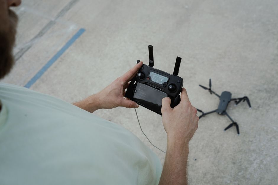 Adult male handling a drone controller, preparing a drone for takeoff on an outdoor surface.