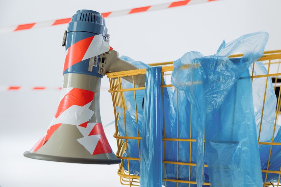 A shopping cart with a megaphone and plastic bags highlights themes of consumerism and activism.