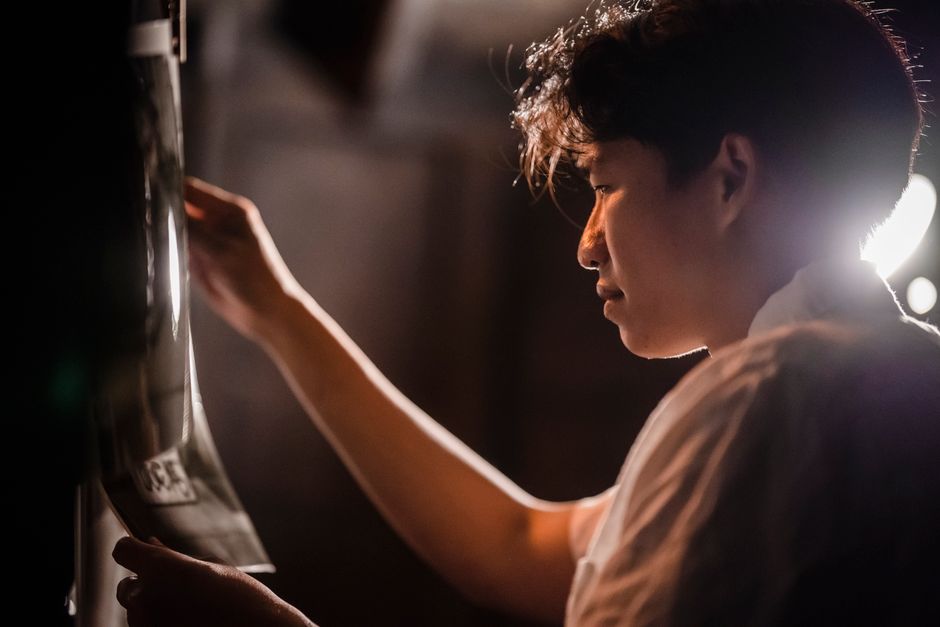 Young photographer attentively examining a photograph in a dimly lit studio setting.