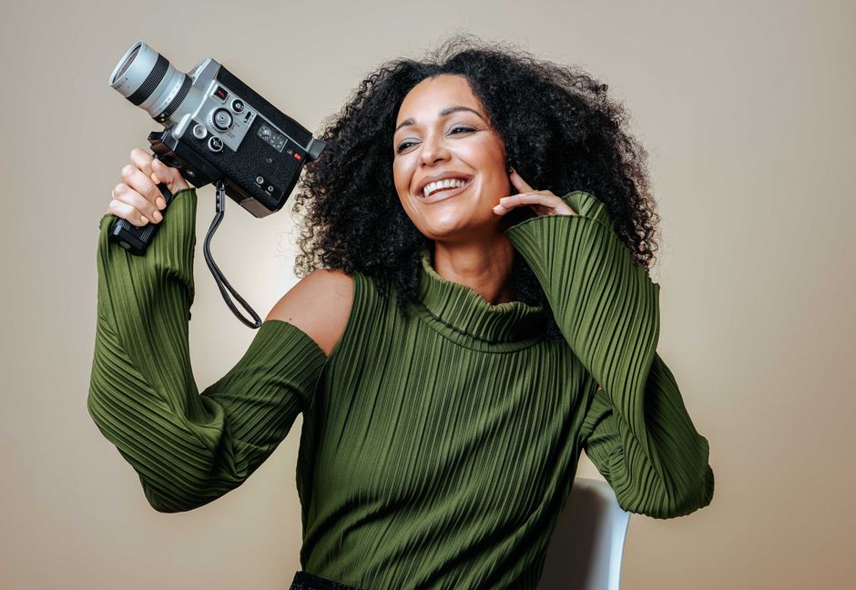 Joyful woman with curly hair holds a vintage camera, showcasing a blend of modern style and nostalgia.