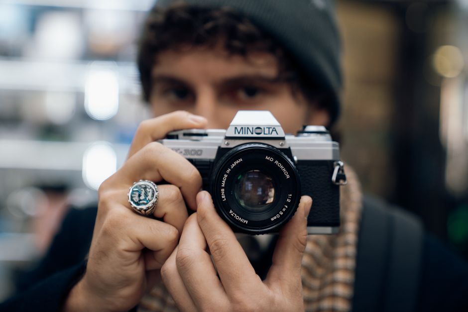 Close-up of a person holding a classic Minolta film camera with focus on lens.