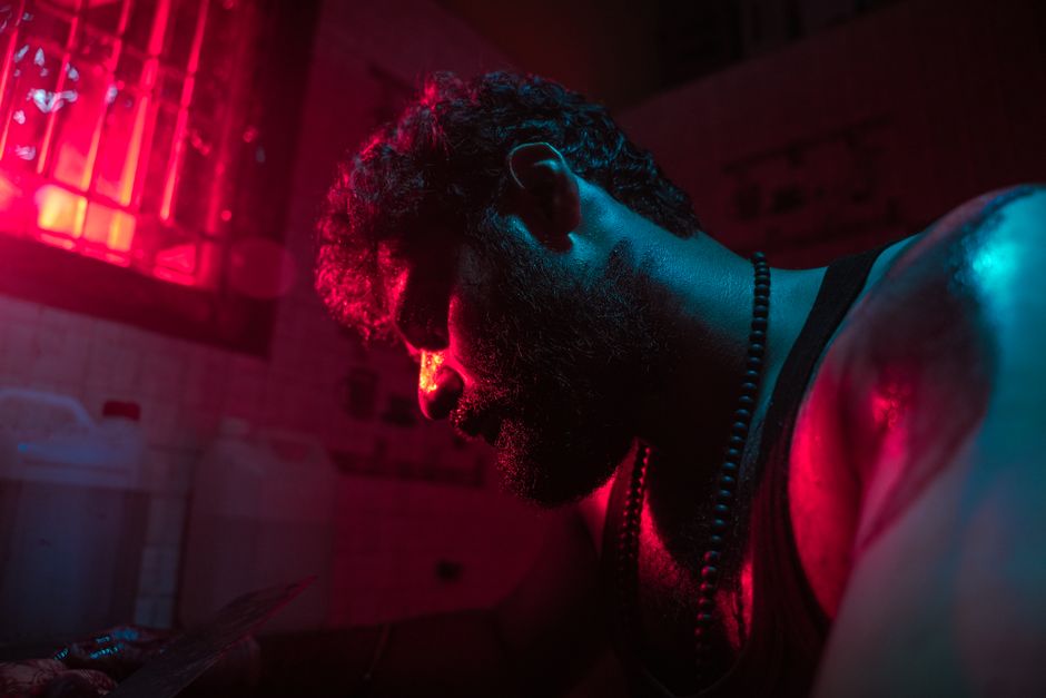Close-up of a man's pensive pose under dramatic red lighting indoors.
