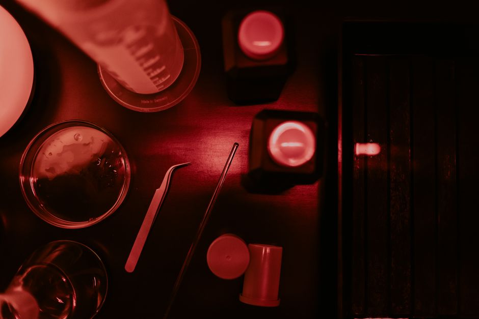 Close-up of darkroom equipment under red lighting, featuring flasks and tweezers.